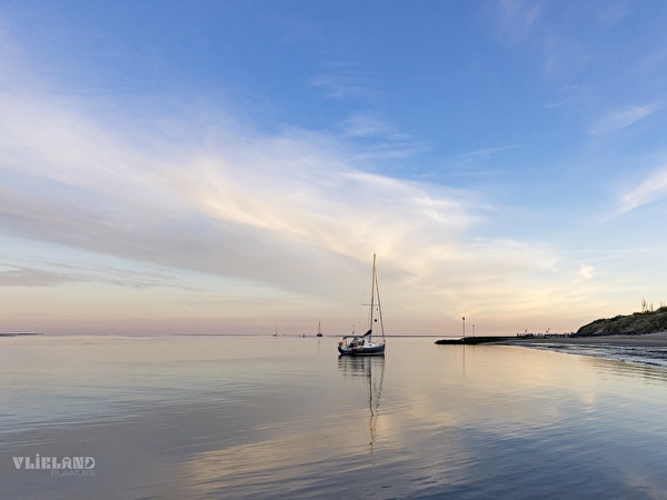 Foto van een spiegelgladde zee met een zeilbootje bij zonsondergang